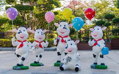 公園一群拿氣球的玻璃鋼卡通奶牛雕塑